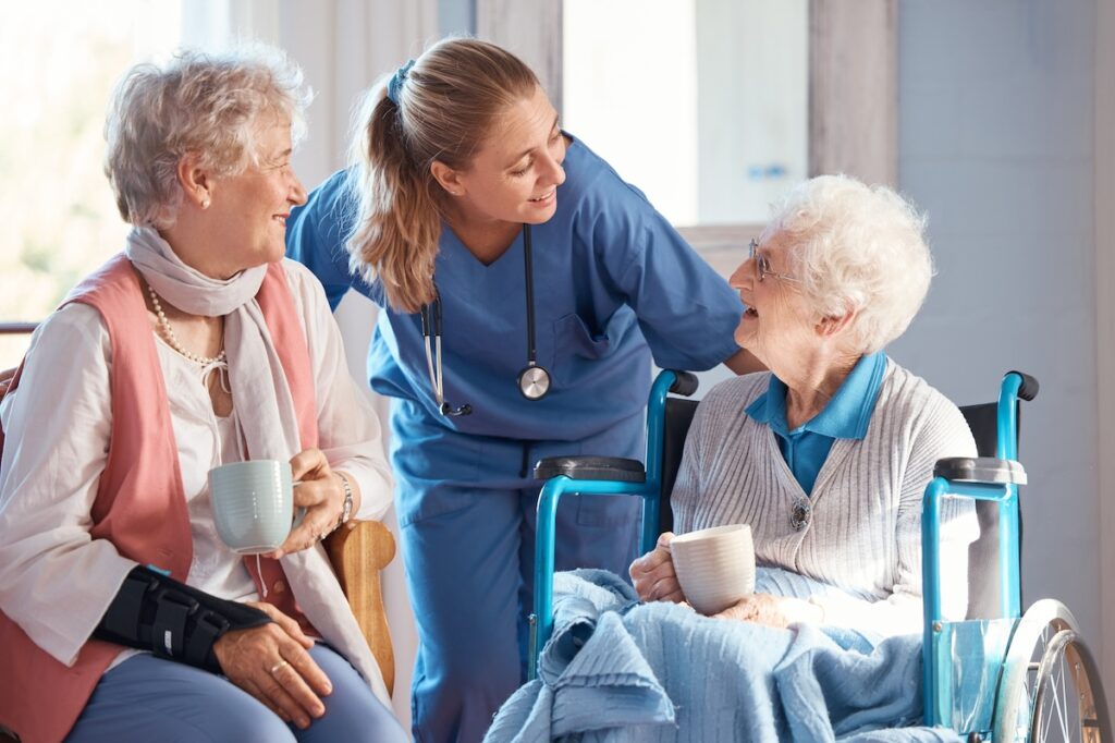 Nursing home, care and nurse with senior women doing healthcare checkup, examination or consultation. Medical, conversation and elderly woman in wheelchair consulting a doctor at retirement facility.